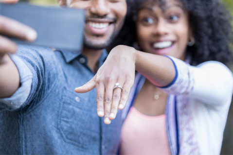 man and woman taking selfie with woman displaying engagement ring