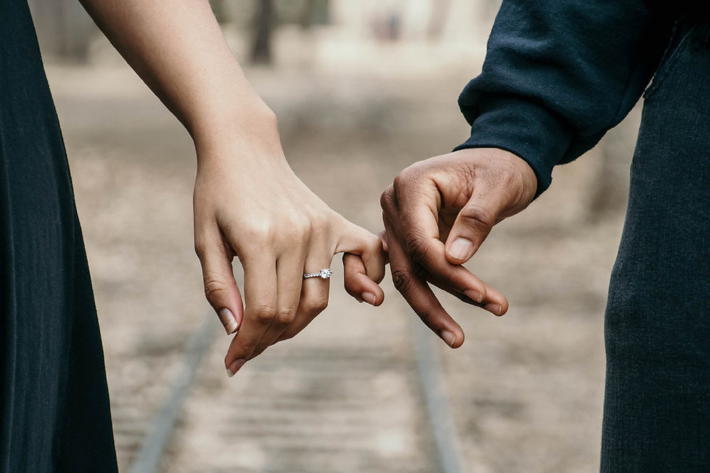couple holding pinkies with engagement ring by railroad track